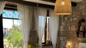 A bedroom with a large bed, a hanging light fixture, a nightstand with a lamp, and a view of the outside balcony. - Ionia Liberty Stone Hotel (Foça)