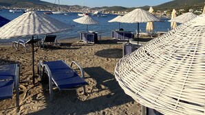 A beach with sun loungers and umbrellas, a clear sky, and boats in the water. - Ionia Liberty Stone Hotel (Foça)