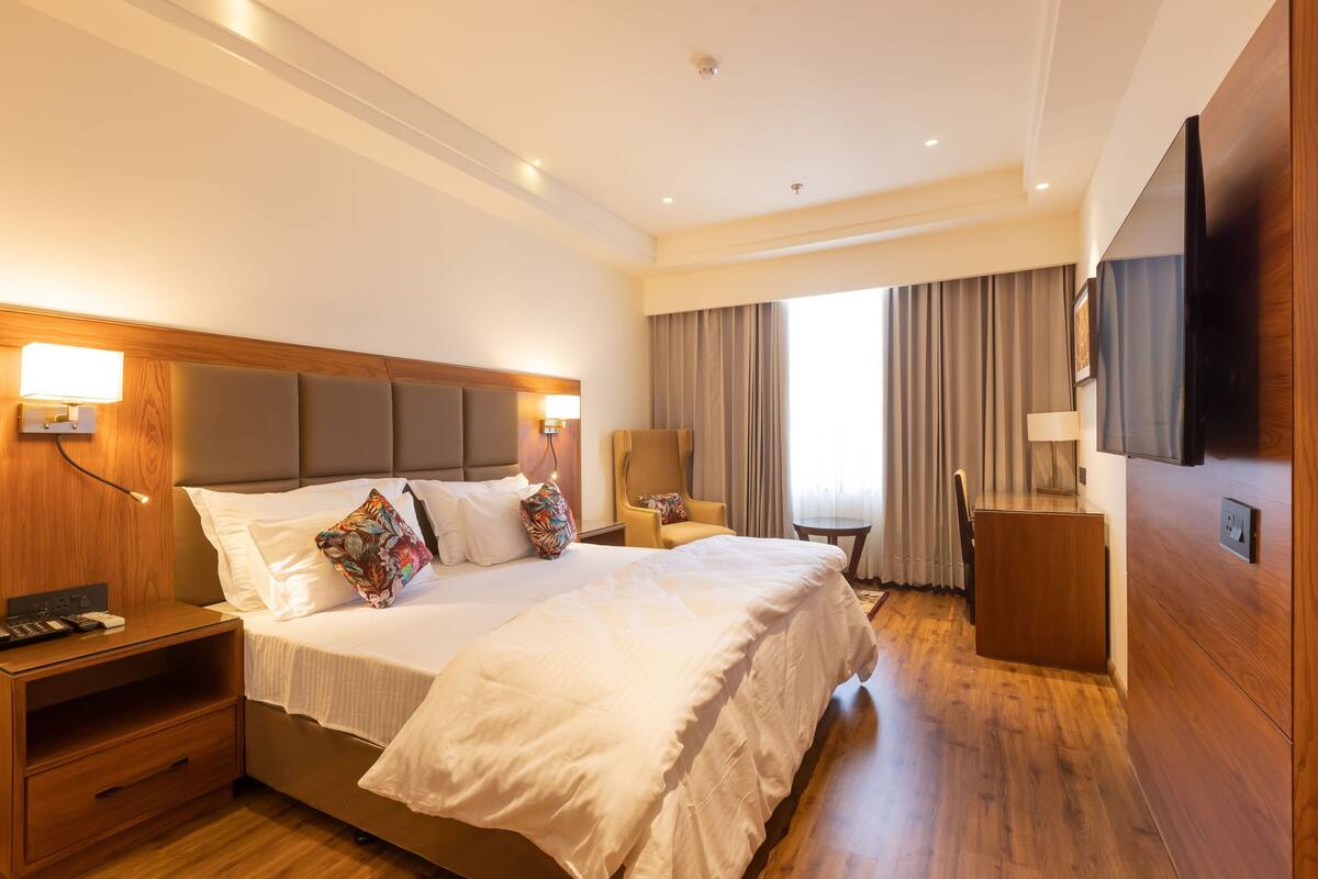 Ein Hotelzimmer mit einem großen Bett, Nachttischen, einem Fernseher und Blick ins Freie.