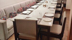 Uma sala de conferências com uma mesa comprida preparada para uma reunião, rodeada por cadeiras e um sofá com almofadas florais.