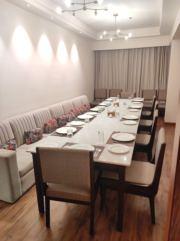 Un salón de conferencias con una larga mesa dispuesta para una reunión, rodeado de sillas y un sofá con cojines estampados.