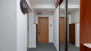 Ein Flur mit einer Holztür, einer Wanduhr und einem Spiegel, der die Tür widerspiegelt.