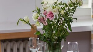 Ein Esstisch ist gedeckt mit Tellern, Gläsern und einer Blumenvase.