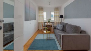 Ein moderner, kompakter Wohnraum mit grauem Sofa, einem Esstisch mit Stühlen und einem kleinen Beistelltisch.