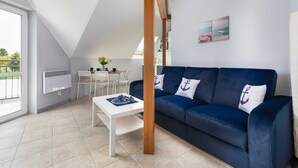 A modern living room with a blue sofa, white table, and a dining area with chairs. - Family Apartment for 6 Persons | Close to the Beach and Parking (Pobierowo)