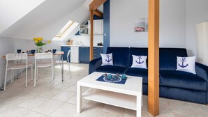 A compact living space with a dining area, a sofa with anchor-themed cushions, and a kitchen in the background. - Family Apartment for 6 Persons | Close to the Beach and Parking (Pobierowo)