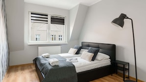 Un dormitorio con cama, mesita de noche, lámpara de pie, ventana con persianas y radiador.