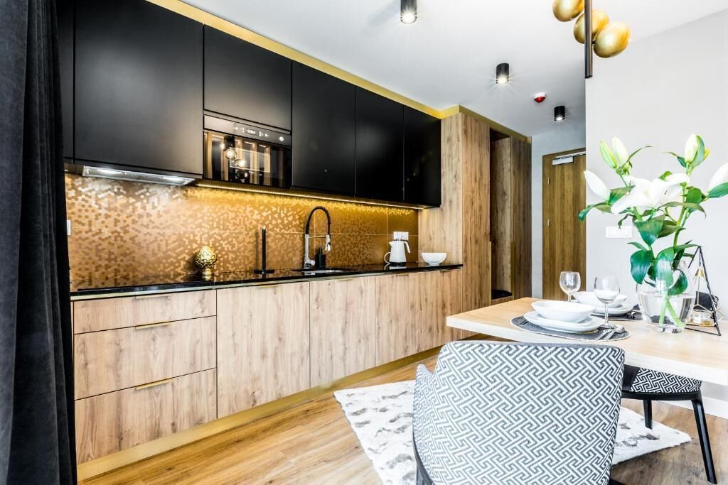 Une cuisine moderne avec des armoires noires, un plan de travail en bois et une cuisinière intégrée. On y trouve un coin repas avec une table et des chaises, ainsi qu’une plante posée sur la table.