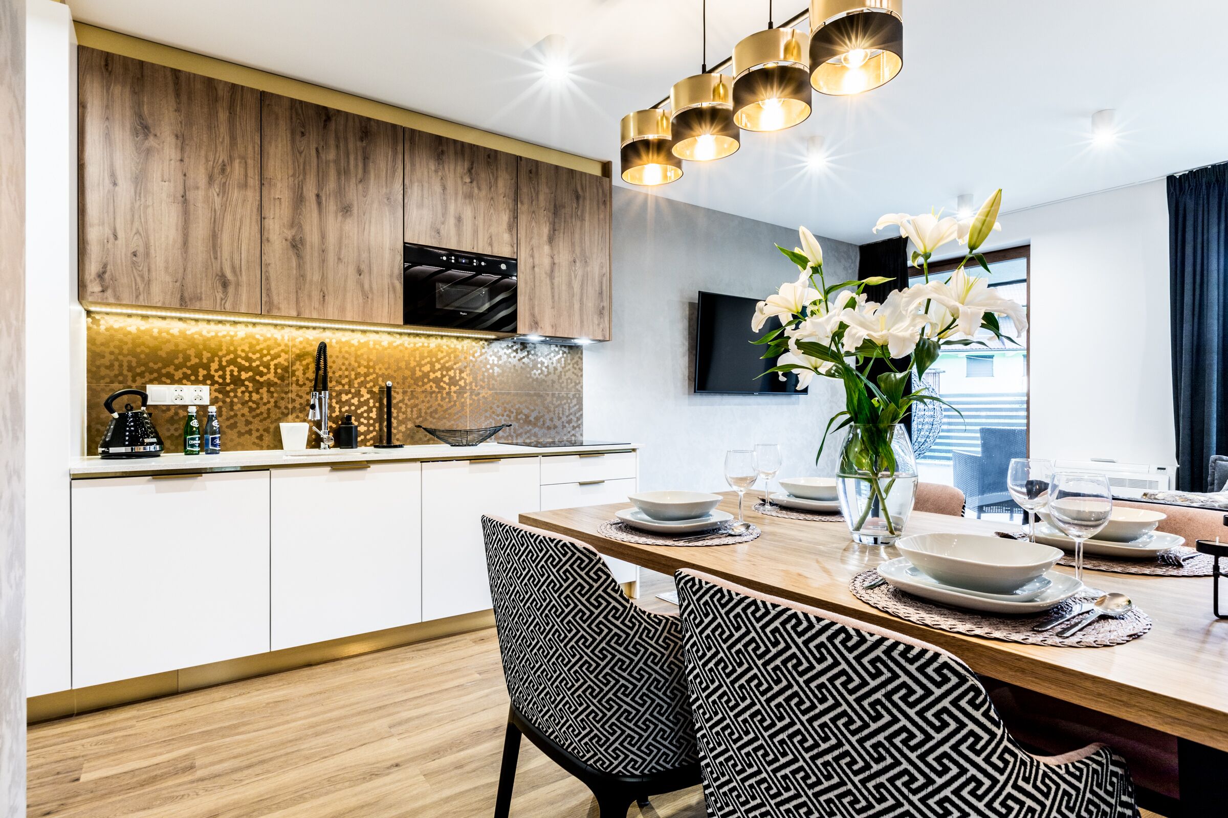 A modern kitchen with wooden cabinets, a built-in oven, and a dining area with a wooden table set for four.