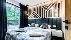 Un dormitorio moderno con una cama grande, cabecero con diseños geométricos, mesitas de noche y vistas al exterior con vegetación.