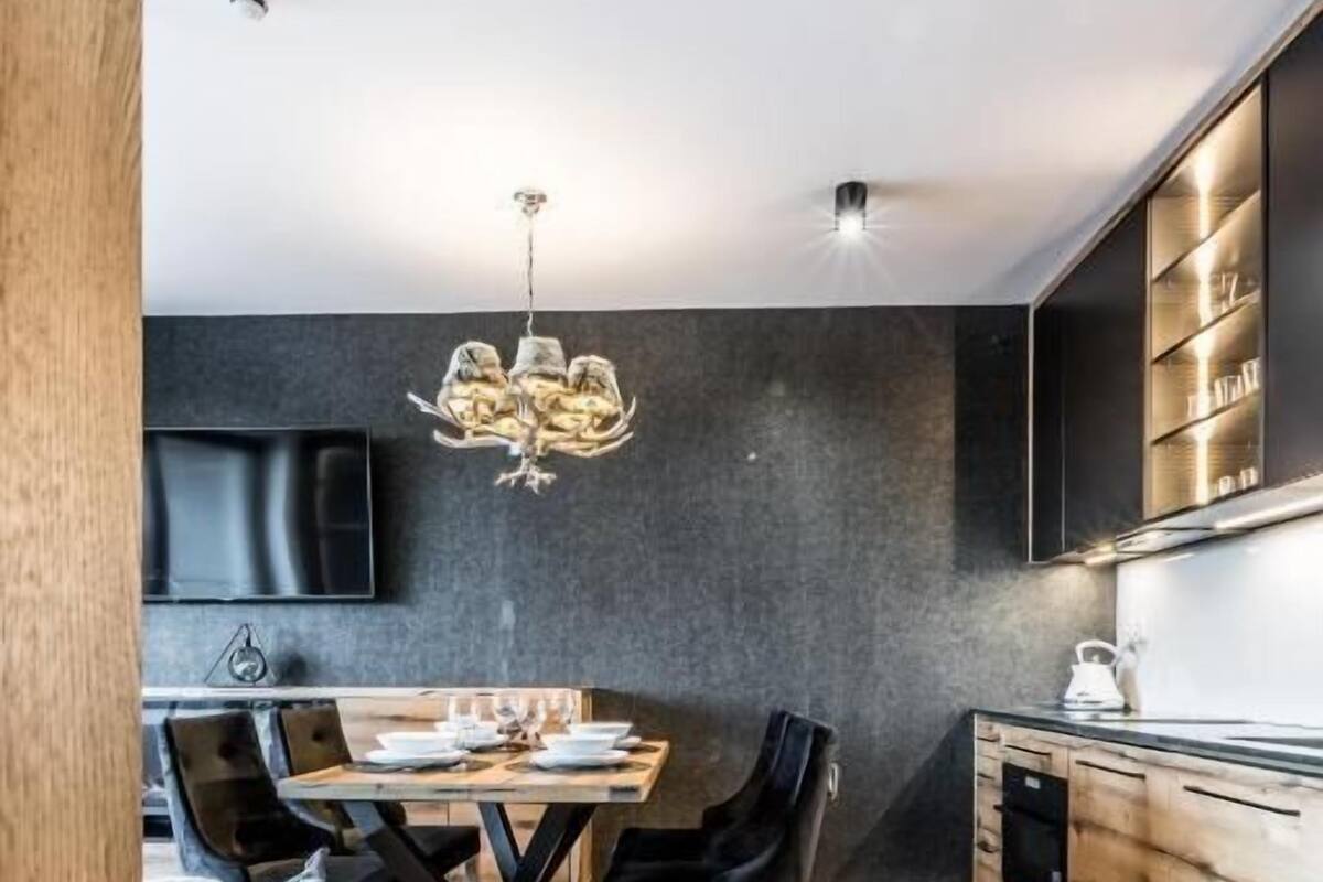 Una cocina moderna con comedor, que presenta suelo de madera, paredes oscuras y una araña.