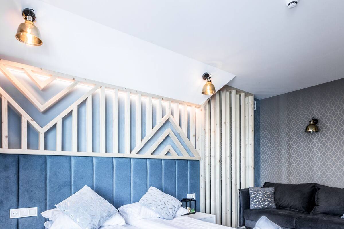 Una habitación de hotel moderna con una cama grande, un sofá oscuro y una pared con estampado.