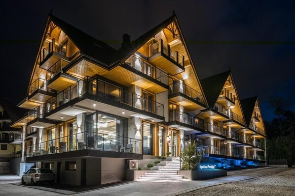 A multi-story hotel with a modern design, featuring balconies, large windows, and a well-lit entrance. - Aparthotel Prestige  (Zakopane)