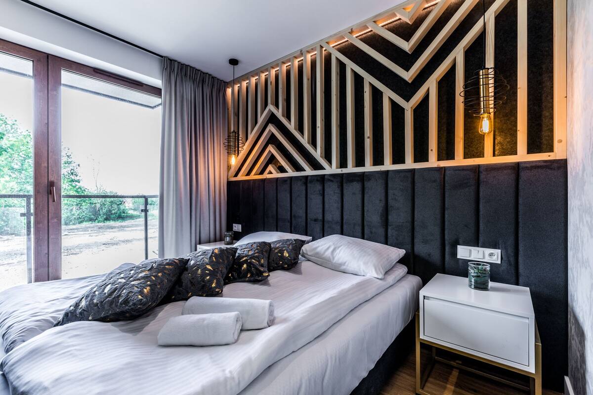 Un dormitorio moderno con una cama grande, una mesita de noche y una lámpara fijada a la pared.