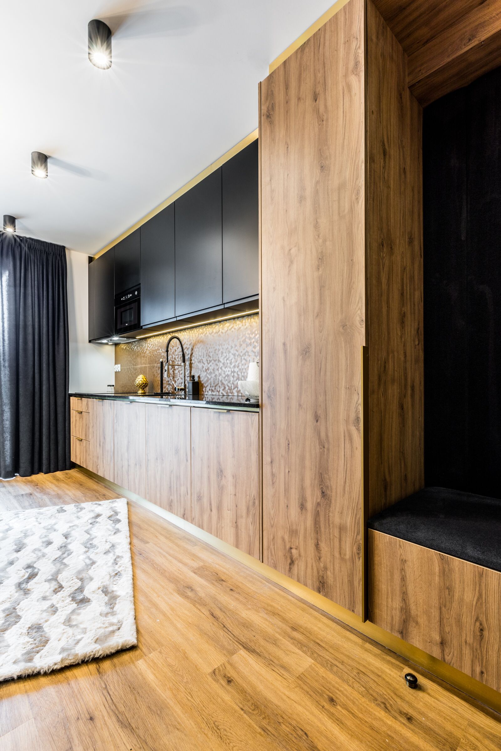 A modern kitchen with wooden cabinetry, a black countertop, and a stainless steel sink.