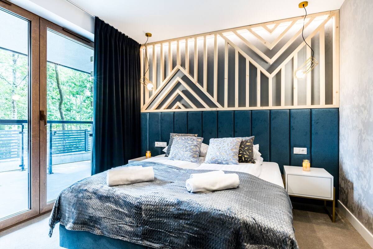 Un dormitorio moderno con una cama grande, vistas al exterior y un diseño geométrico en la pared.