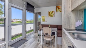 Een moderne keuken met een ingebouwde kookplaat, een eethoek met een bank, en grote ramen met uitzicht op de straat.