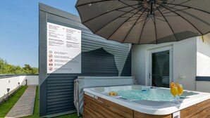 Een hottub met twee glaasjes jus d'orange, een houten terras en een overdekt gedeelte met een bord.