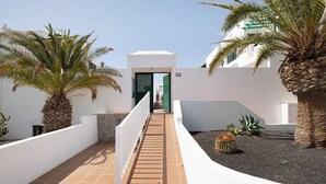 Un corridoio con palme, un pavimento piastrellato e un edificio bianco con un cancello verde.