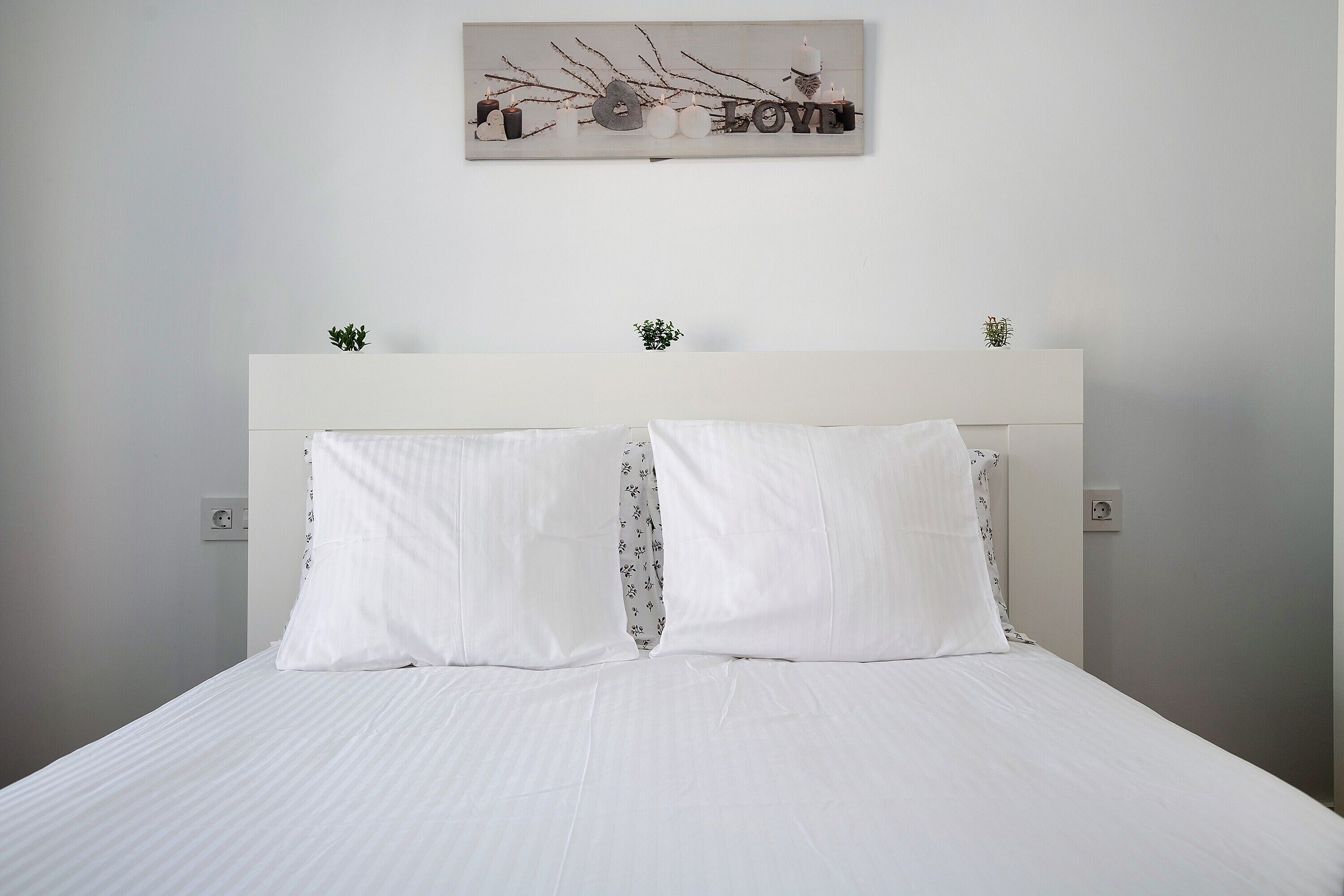 A neatly made bed with white linens and two pillows, a white headboard, and a wall-mounted decoration above.