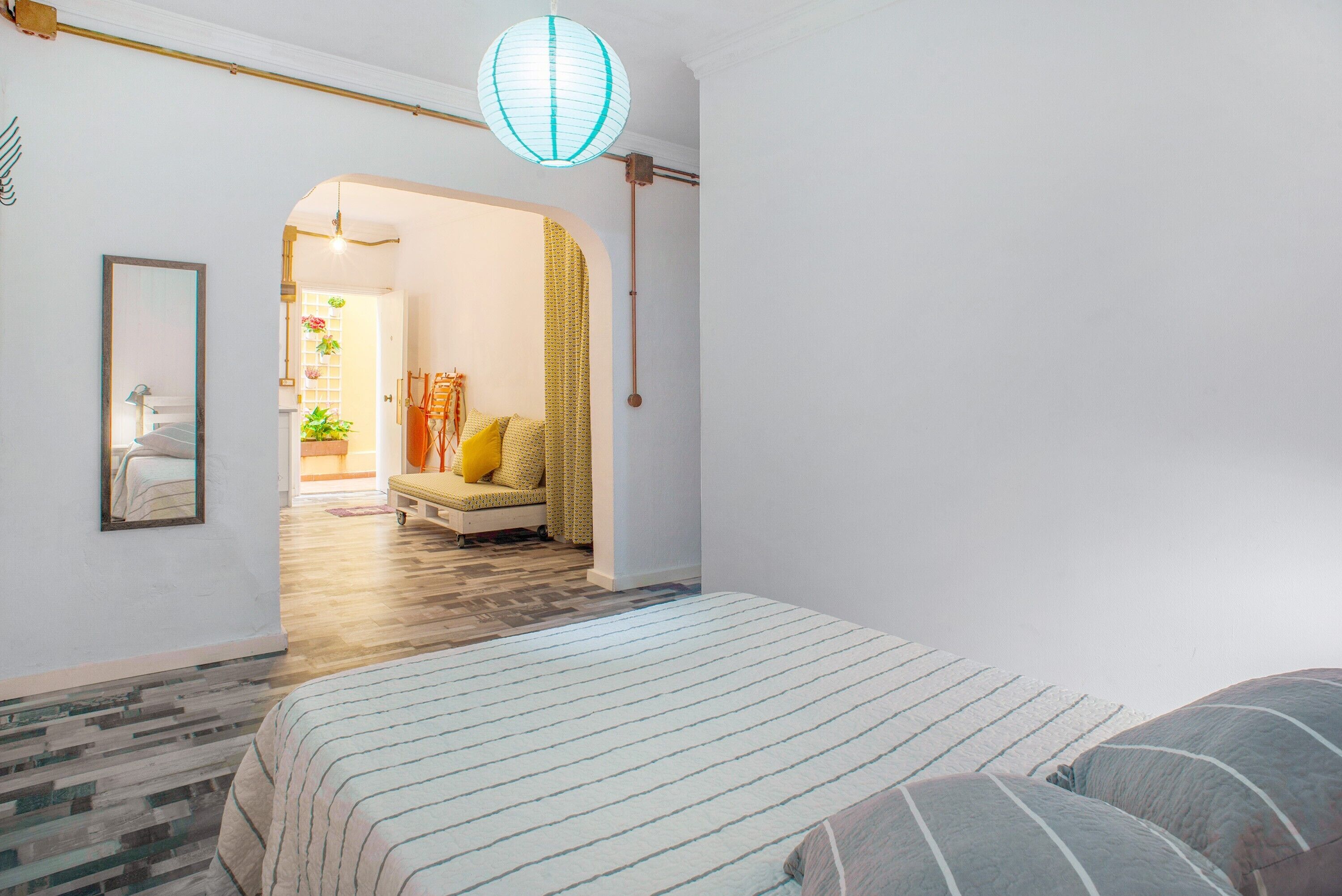 A bedroom with a bed, a mirror, a hanging light fixture, and a doorway leading to another room.