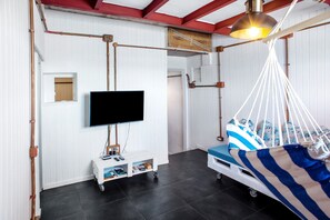 A room with a television mounted on the wall, a white cabinet with drawers, a hanging chair with a striped cushion, and a ceiling light fixture.