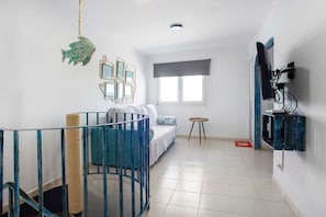 Une chambre avec un lit, une petite table, un téléviseur fixé au mur et une fenêtre avec un store.