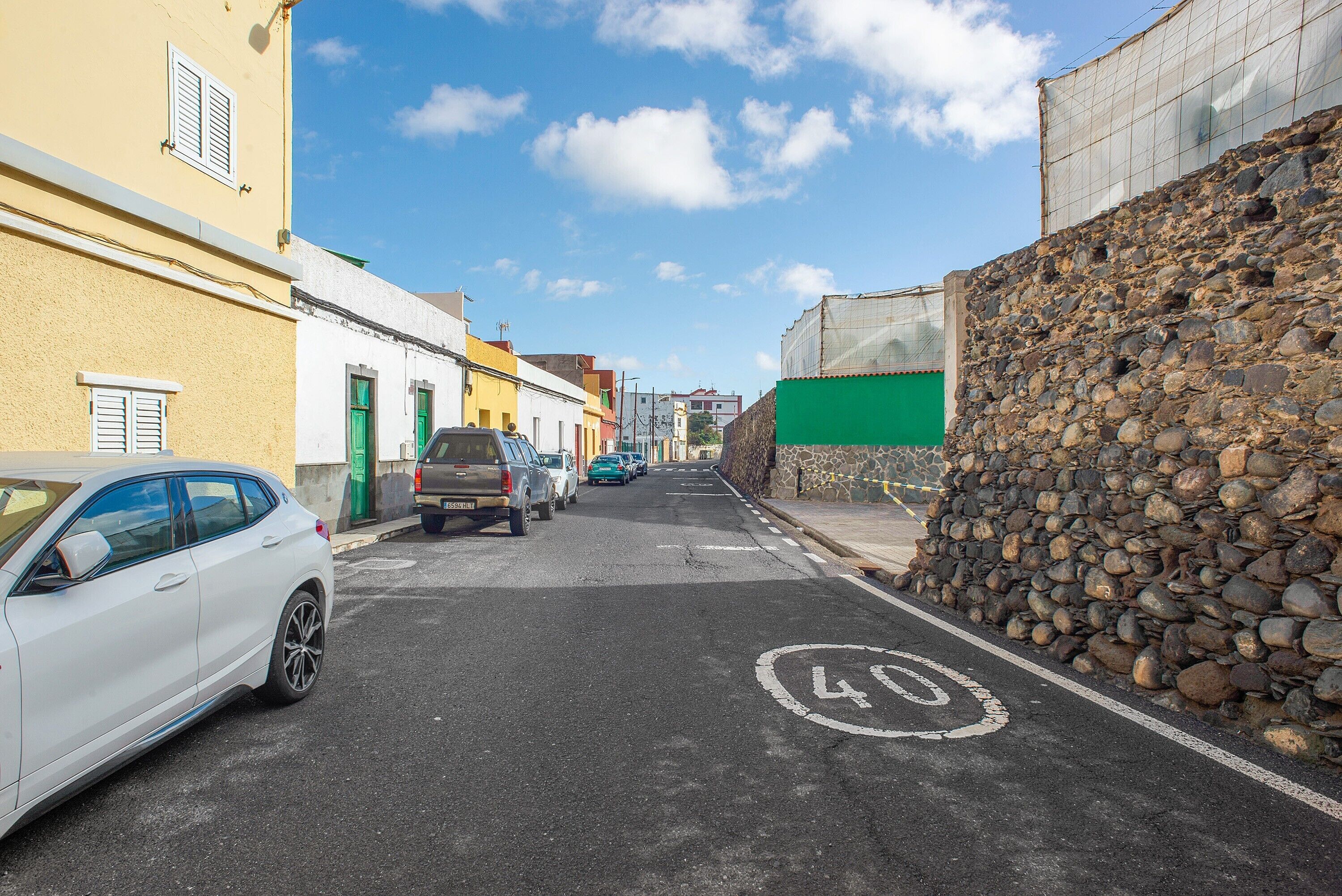 A narrow street with parked cars, a speed limit sign, and buildings with distinct architectural styles.