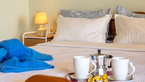 Ein ordentlich bezogenes Bett mit weißen Leinentüchern, einem blauen Handtuch und einem Tablett mit zwei weißen Tassen und einem kleinen Behälter.