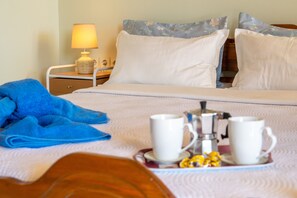 A neatly made bed with white linens, a blue towel, and a tray with two white cups and a small container.