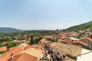 A town with a prominent clock tower, terracotta-roofed buildings, and a hilly backdrop.