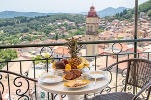 A balcony with a table set for breakfast, a clock tower, and a view of a town. - Pavlos & Sofia Studio Apartment with Mountain View, Garden and Terrace (Corfu)