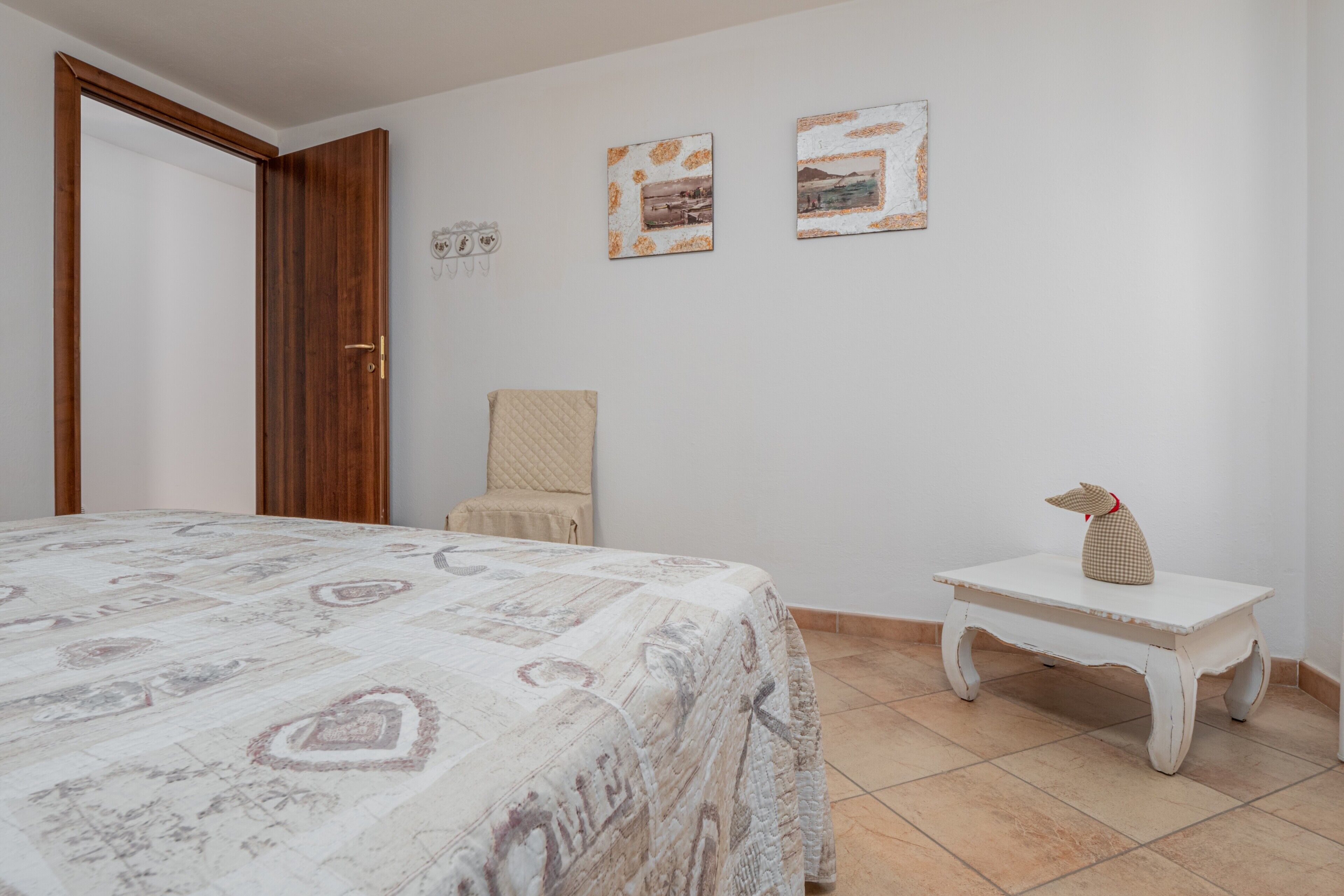 A bedroom with a bed, a chair, a small table, and two framed pictures on the wall.