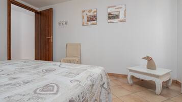 A bedroom with a bed, a chair, a small table, and two framed pictures on the wall.