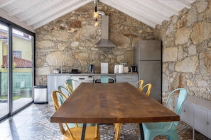 A rustic kitchen with a stone wall, a wooden table, and a view through a glass door.
