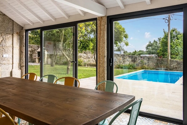 A dining area with a wooden table and chairs, large sliding glass doors leading to a swimming pool.