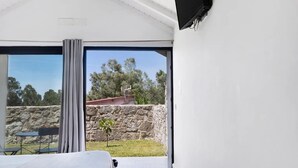Une chambre dotée d’un lit, d’un téléviseur fixé au mur et d’une grande fenêtre donnant sur l’extérieur.