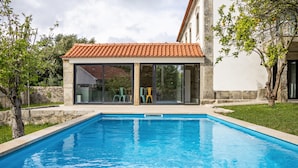Une piscine dotée d’une structure de toit en carrelage, d’un mur en pierre et d’une zone herbeuse avec des arbres.