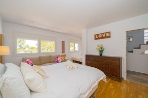 Une chambre avec un grand lit, une commode, un bureau et un panneau mural sur lequel est écrit le mot « AMOUR ».