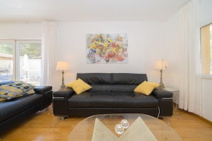 Un salon moderne avec un canapé en cuir noir, une table basse en verre et un tableau abstrait aux couleurs vives accroché au mur.