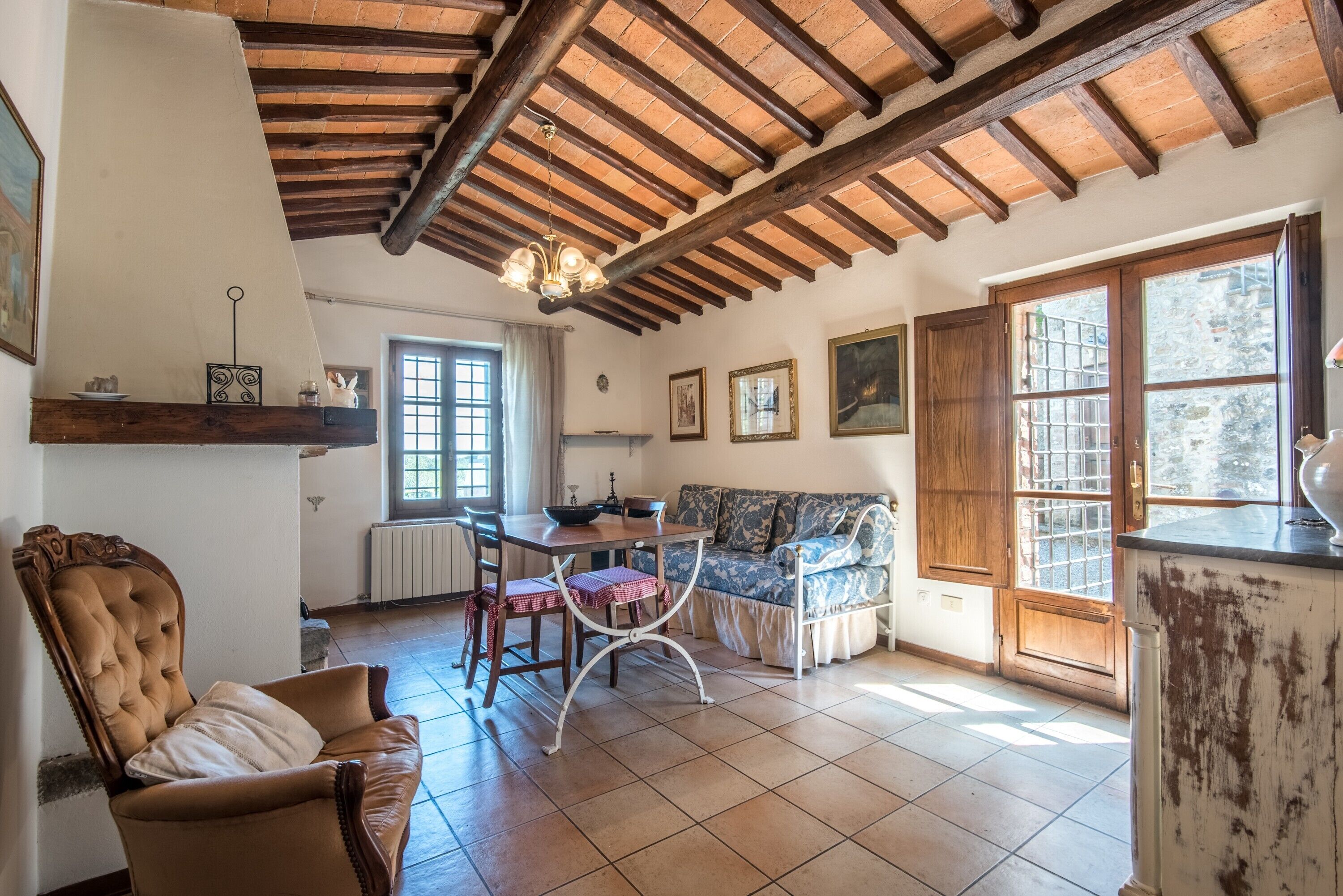 Ein rustikaler Innenraum mit freiliegenden Holzbalken, einem Essbereich mit Tisch und Stühlen, einer Couch und einem Fenster mit Blick.