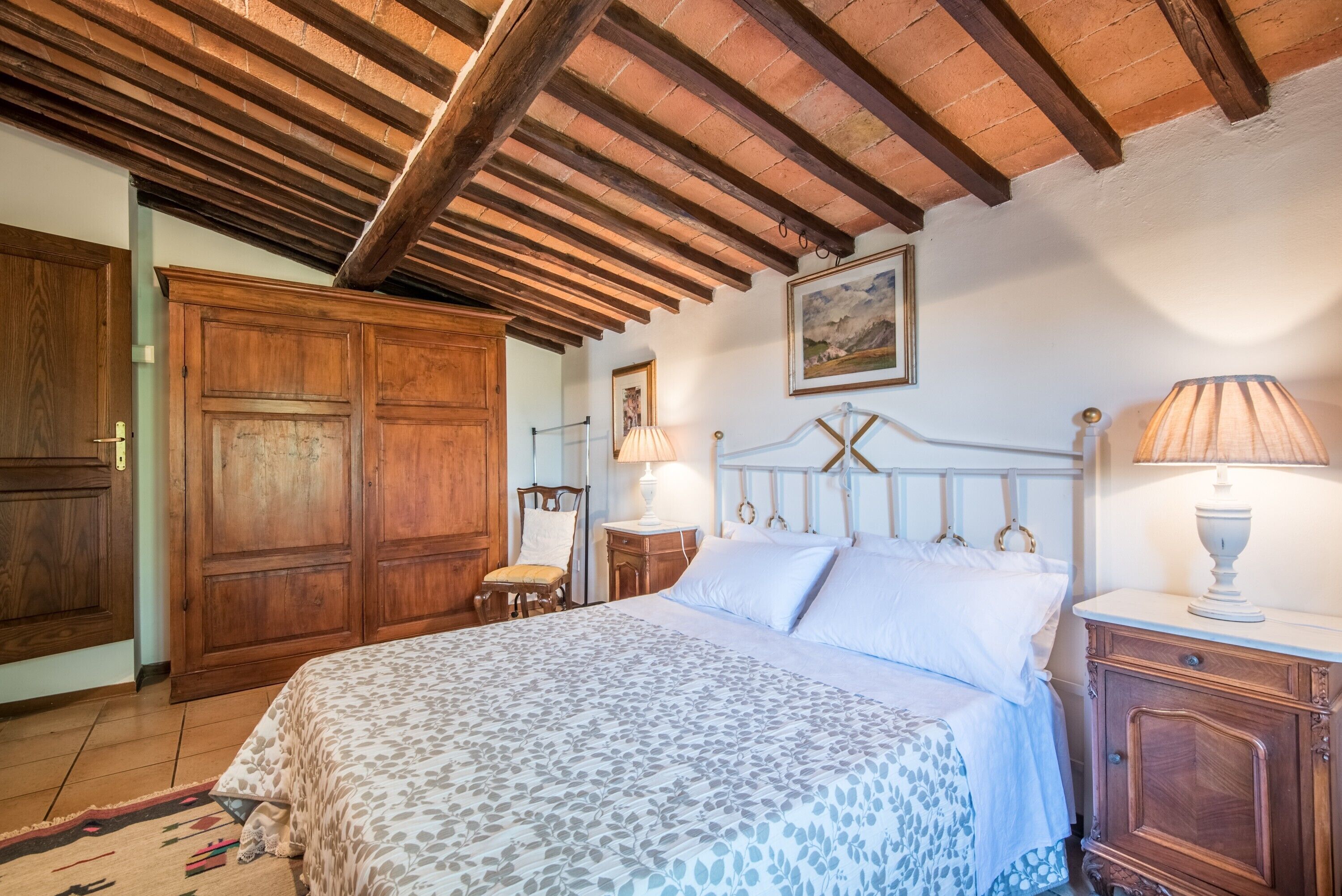 Une chambre à coucher avec un lit, une armoire en bois, un tableau et une lampe.