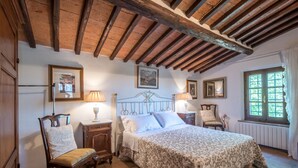 Une chambre à coucher avec un lit, une tête de lit en bois, deux tables de chevet avec des lampes, une chaise et une fenêtre avec des rideaux.