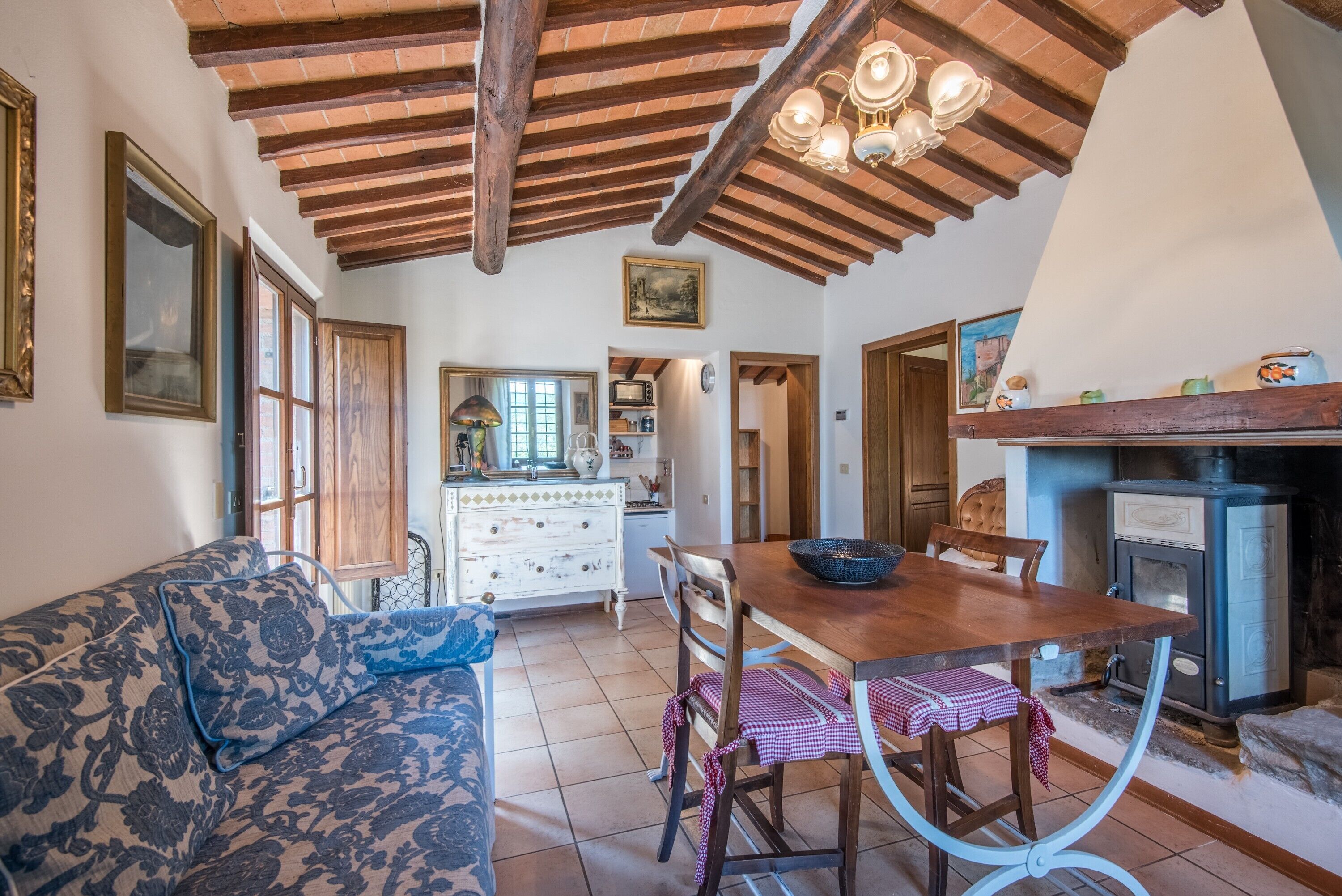 Un interior rústico con techo de madera, una mesa de comedor con sillas, un sofá y una zona de cocina con estufa.
