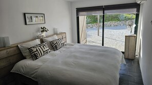 Een slaapkamer met een groot bed, een houten hoofdbord, een schilderij aan de muur en uitzicht op een terras.