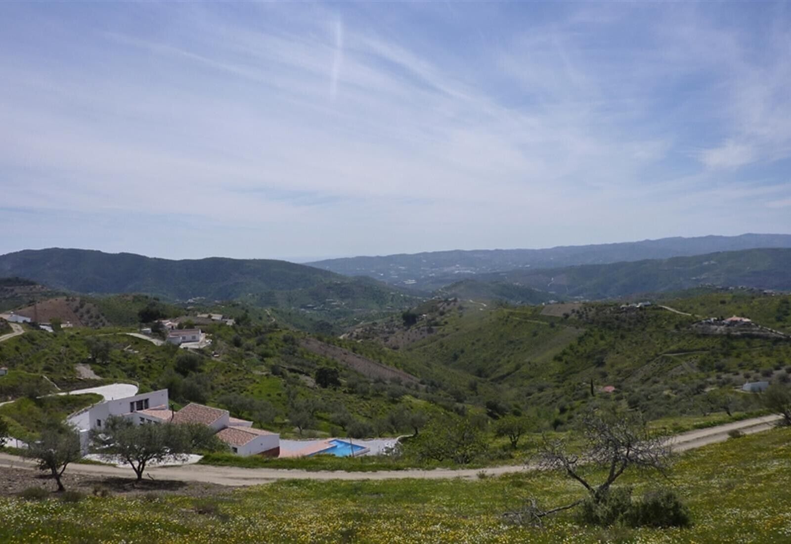 Un paisaje montañoso con algunos edificios, incluyendo una casa blanca con techo rojo y una piscina azul.