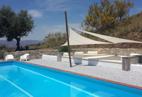 Una piscina con sillas blancas y una zona sombreada.