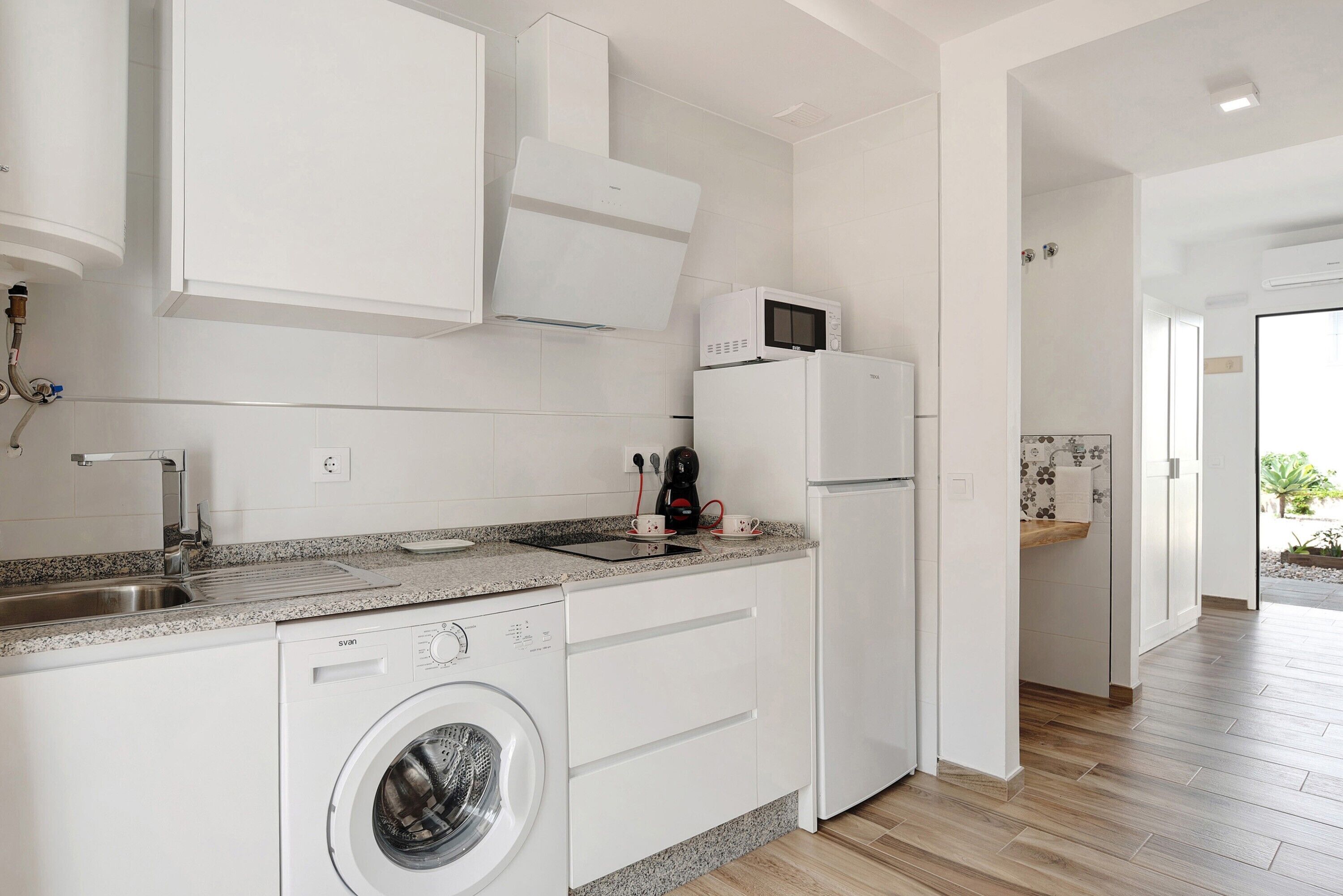 A modern kitchen with a washing machine, microwave, and refrigerator.