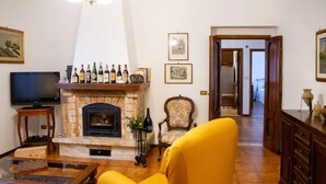 Een woonkamer met een open haard, een televisie en een gele fauteuil.
