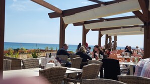 Ein Essbereich im Freien mit Korbmöbeln, Tischen und Blick auf das Meer.